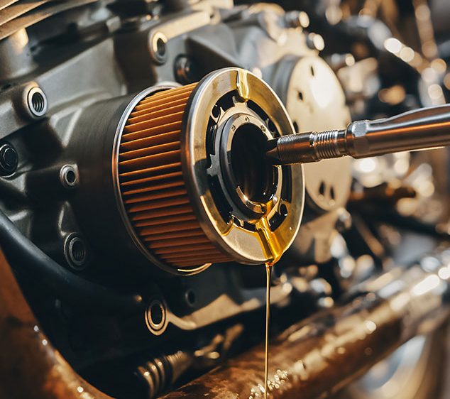 Öl wird in einen Motorradmotor eingefüllt, Filter und Werkzeug sind sichtbar.